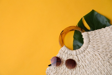 Stylish straw bag and sunglasses on yellow background, flat lay with space for text. Summer accessories