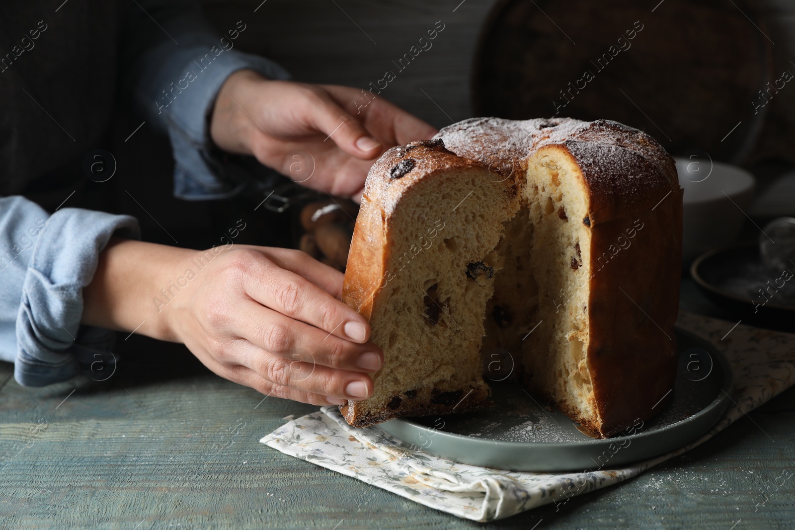 Photo of Woman taking slice of delicious Panettone cake with powdered sugar at light blue wooden table, closeup. Traditional Italian pastry