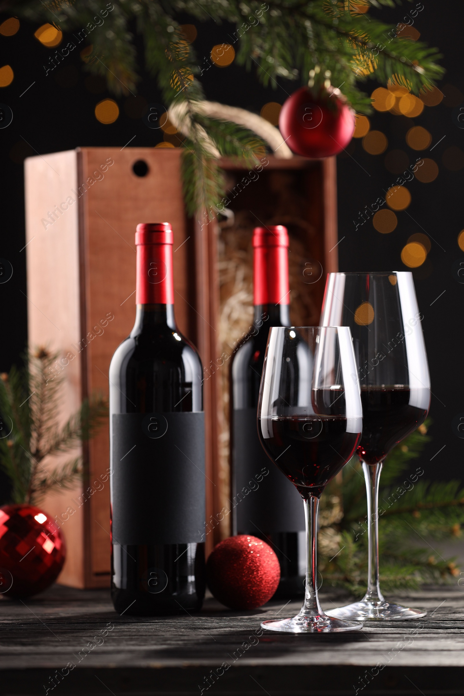 Photo of Bottles of wine, glasses, wooden boxes, fir twigs and red Christmas balls on table