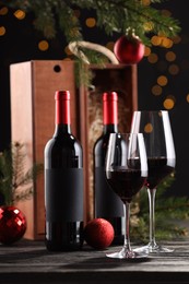 Bottles of wine, glasses, wooden boxes, fir twigs and red Christmas balls on table