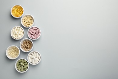 Different vitamin pills in bowls on grey background, flat lay. Space for text