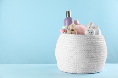 Photo of Basket with baby cosmetic products and accessories on light blue background. Space for text