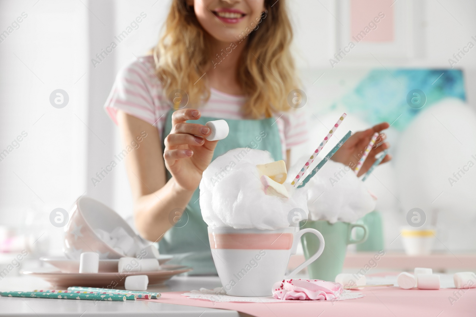 Photo of Young woman decorating cotton candy dessert with marshmallow at table, closeup