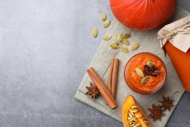 Photo of Jars of pumpkin jam, star anise, cinnamon and fresh pumpkins on grey table, flat lay. Space for text