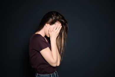 Upset young woman crying against dark background. Space for text