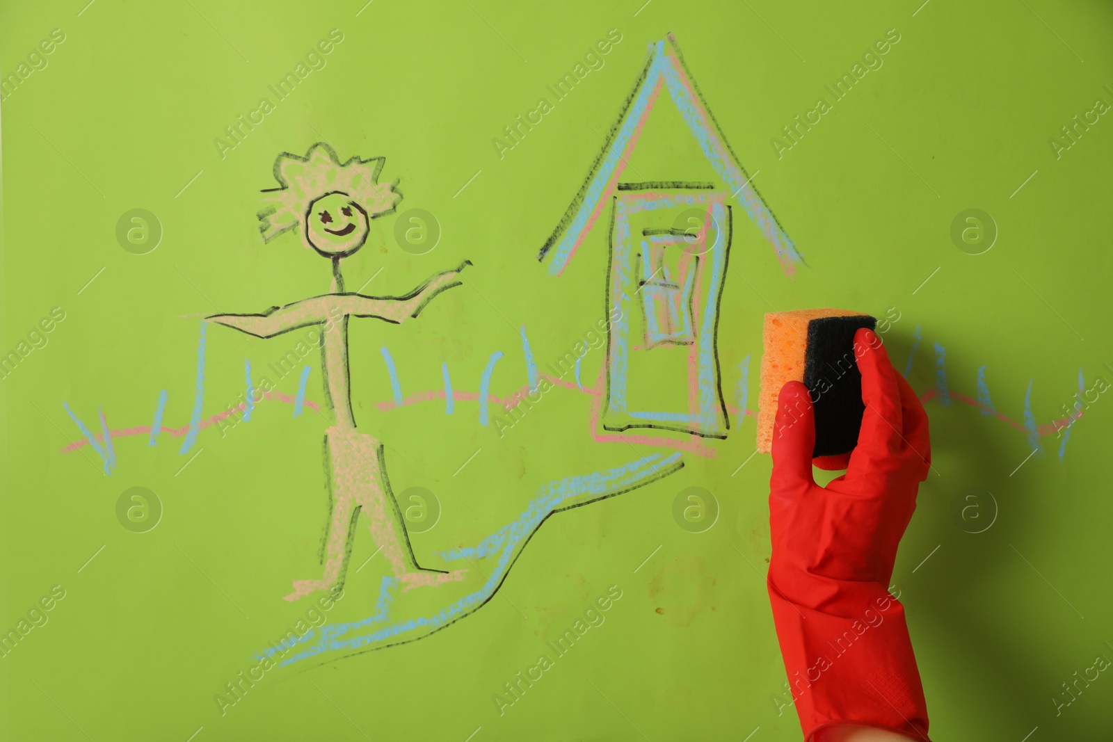 Photo of Woman erasing child's drawing from green wall, closeup