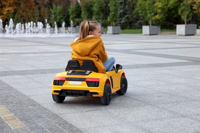 Photo of Cute little girl driving children's car on city street, back view