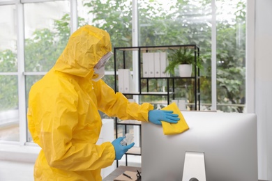 Photo of Janitor disinfecting computer in office to prevent spreading of COVID-19