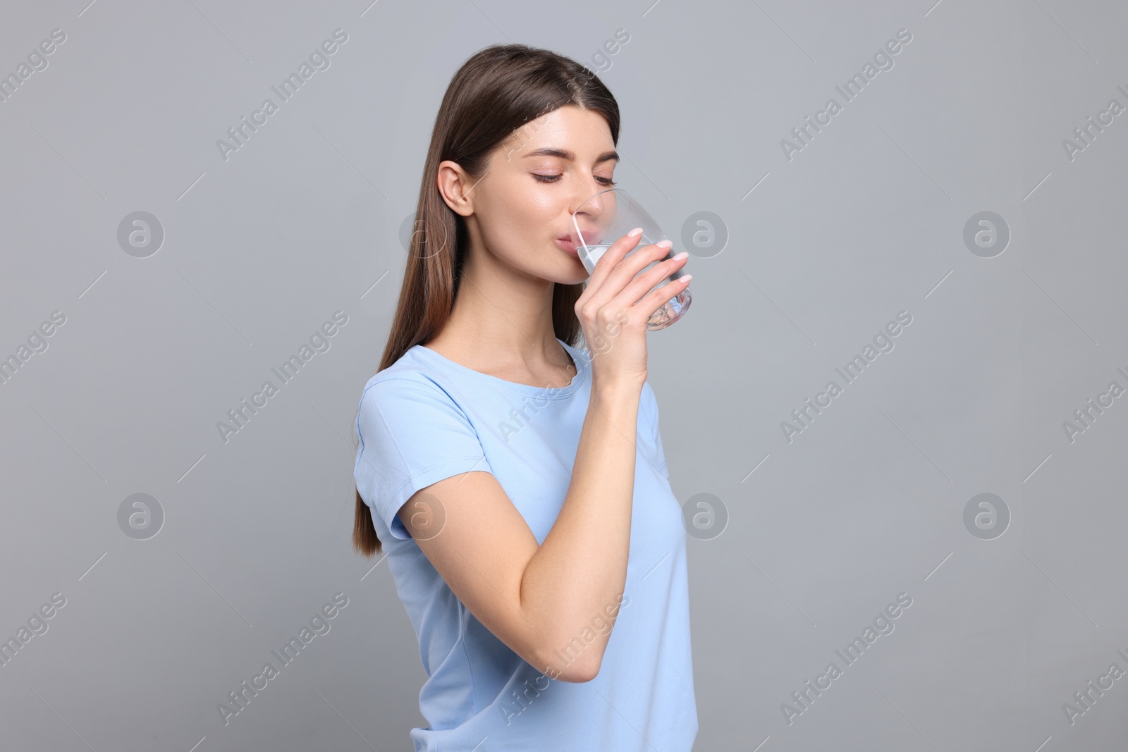 Photo of Healthy habit. Woman drinking fresh water from glass on grey background