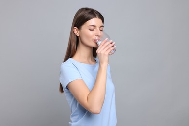 Photo of Healthy habit. Woman drinking fresh water from glass on grey background