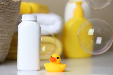 Photo of Bottle of dusting powder and rubber duck on white table, space for text. Baby cosmetic product