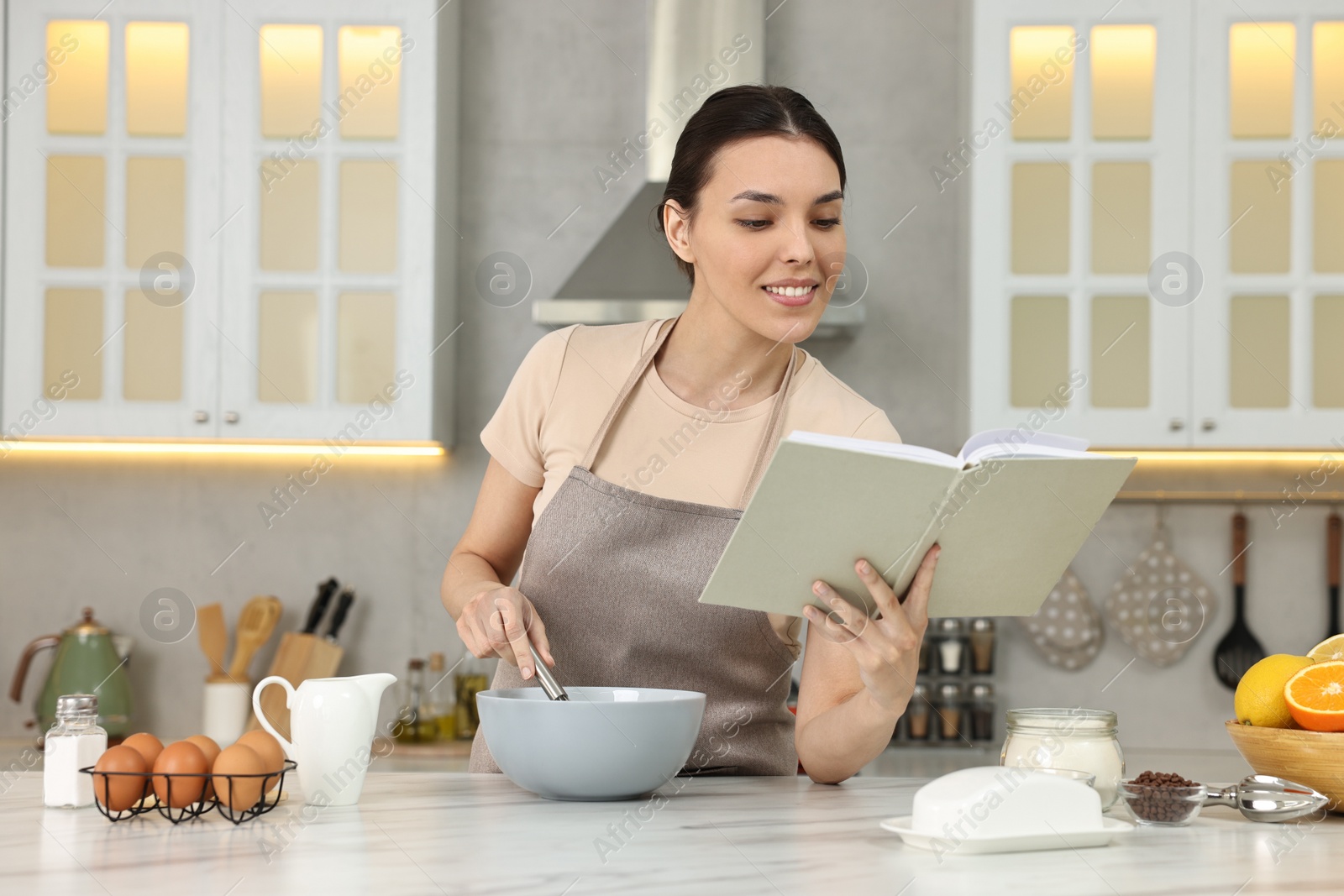 Photo of Young woman with recipe book cooking in kitchen