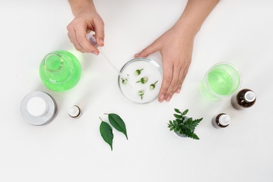 Female dermatologist creating skin care product on white background, top view