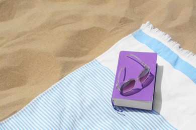 Photo of Beach towel with book and sunglasses on sand, space for text