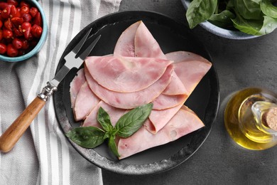 Photo of Tasty ham with basil, olive oil, pickled peppers and carving fork on grey table, flat lay