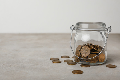 Glass jar with coins on grey table, space for text