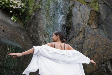 Young woman near beautiful waterfall outdoors, low angle view