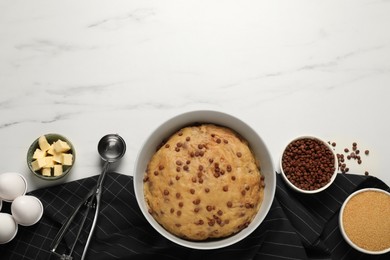 Photo of Bowl with dough and ingredients for cooking chocolate chip cookies on white marble table, flat lay. Space for text