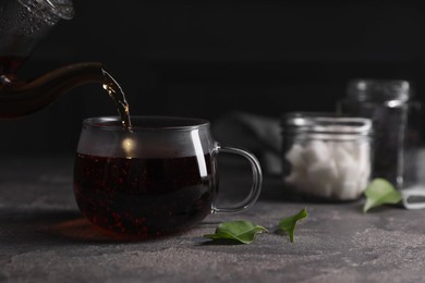 Photo of Pouring hot tea into cup on grey table, closeup