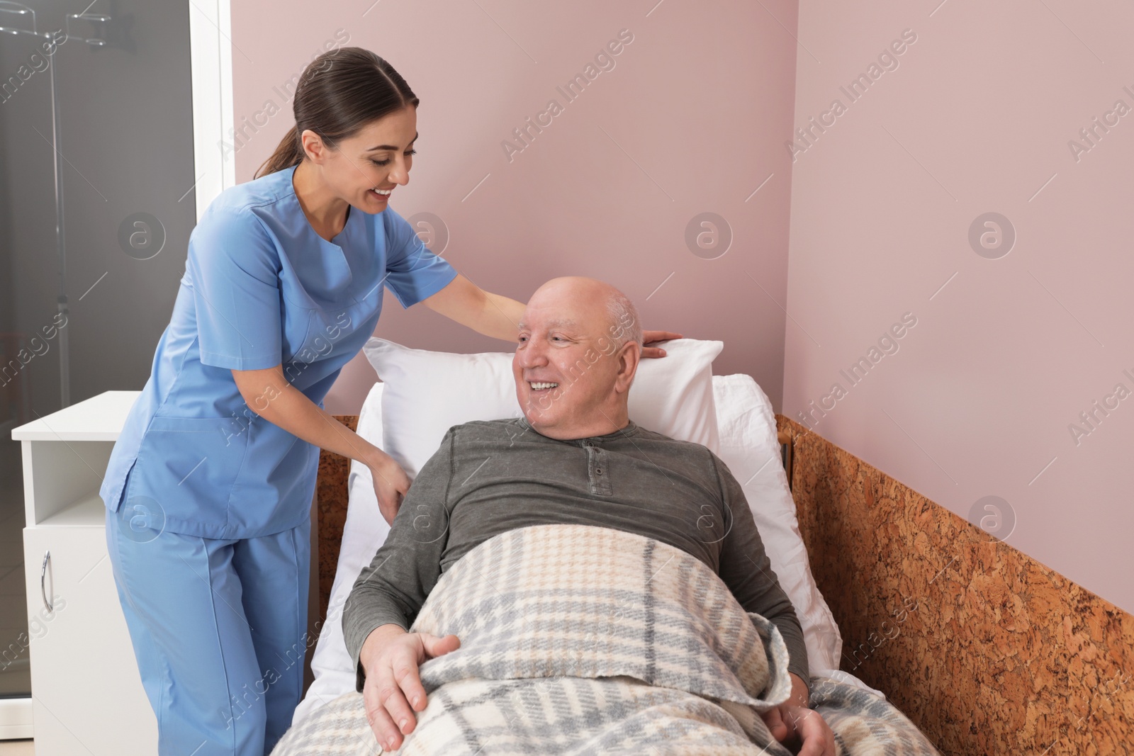 Photo of Nurse assisting senior man on bed in hospital ward