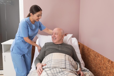 Photo of Nurse assisting senior man on bed in hospital ward