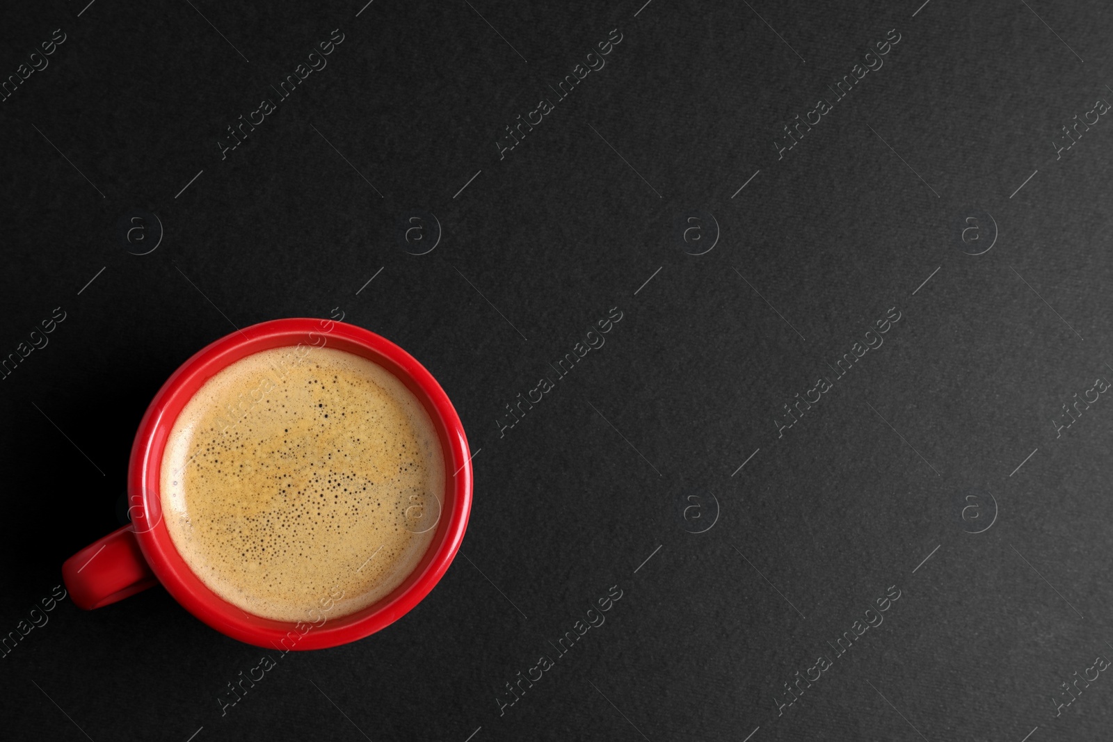 Photo of Red ceramic cup with hot aromatic coffee on black background, top view. Space for text
