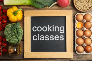 Image of Small chalkboard with inscription Cooking Classes and different fresh products on wooden table, flat lay