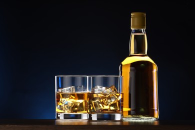 Photo of Whiskey with ice cubes in glasses and bottle on table against dark background
