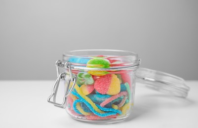 Photo of Tasty jelly candies in open jar on white table