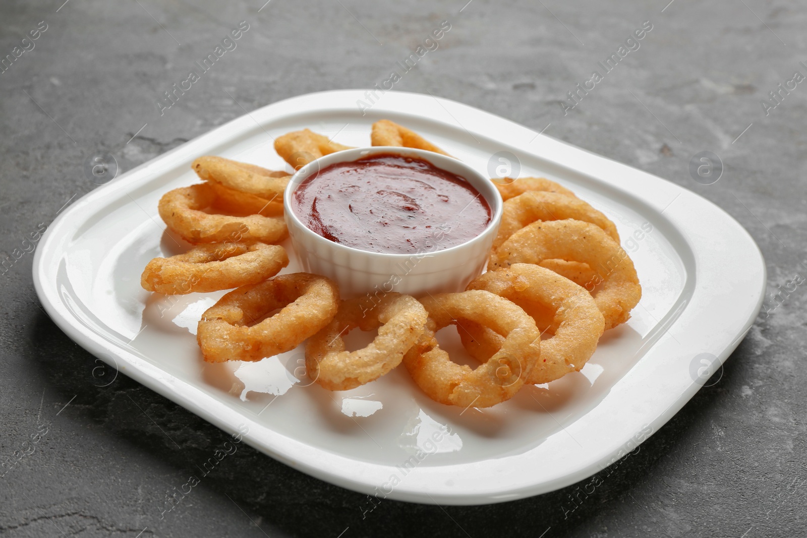 Photo of Plate with fried onion rings and sauce on table