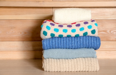 Photo of Stack of winter clothes against wooden background. Space for text