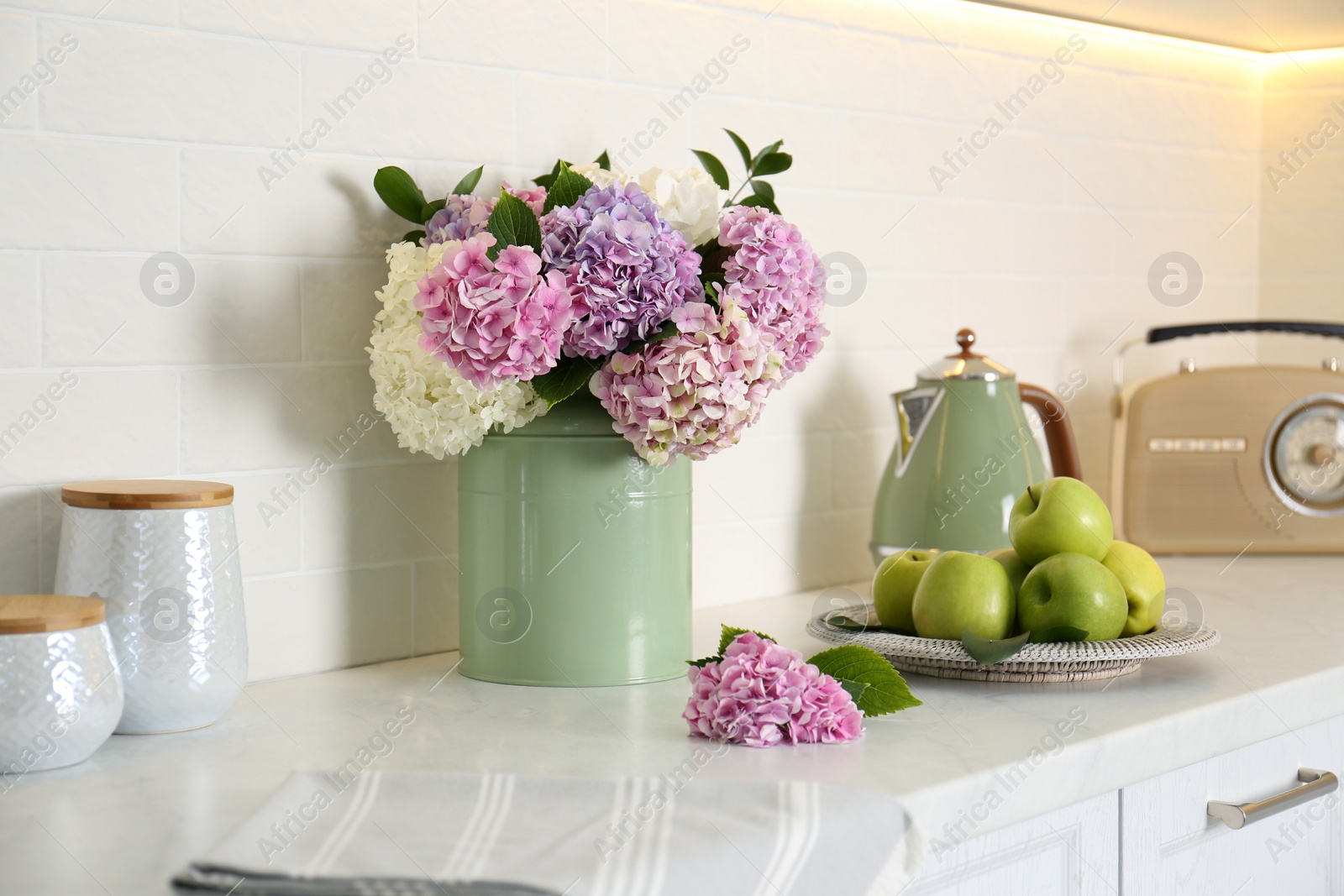 Photo of Beautiful hydrangea flowers, kettle and apples on light countertop