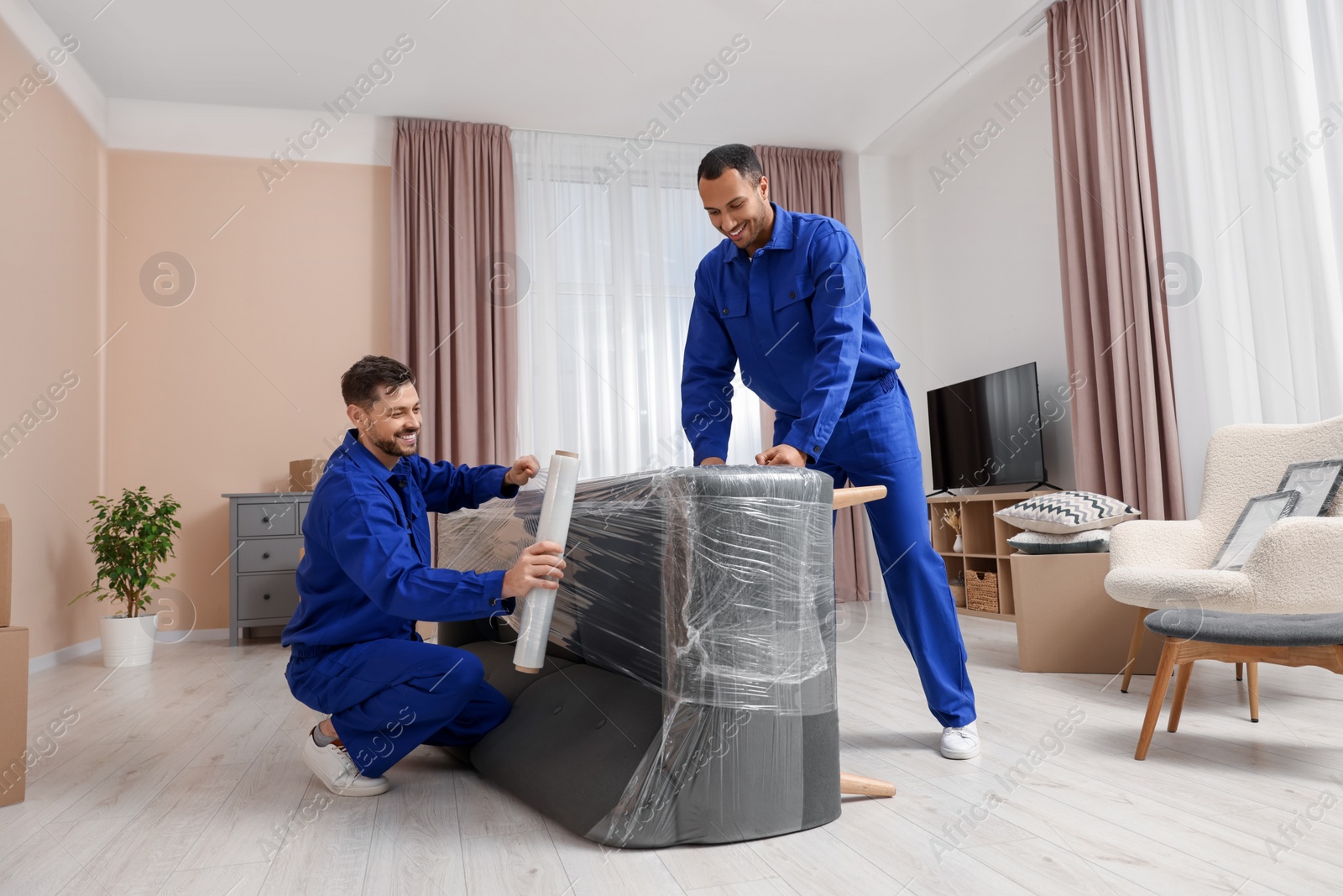 Photo of Male movers with stretch film wrapping sofa in new house