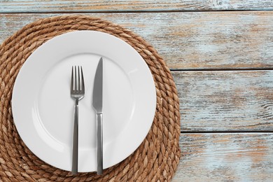 Photo of White plate, fork and knife on wooden table, top view. Space for text