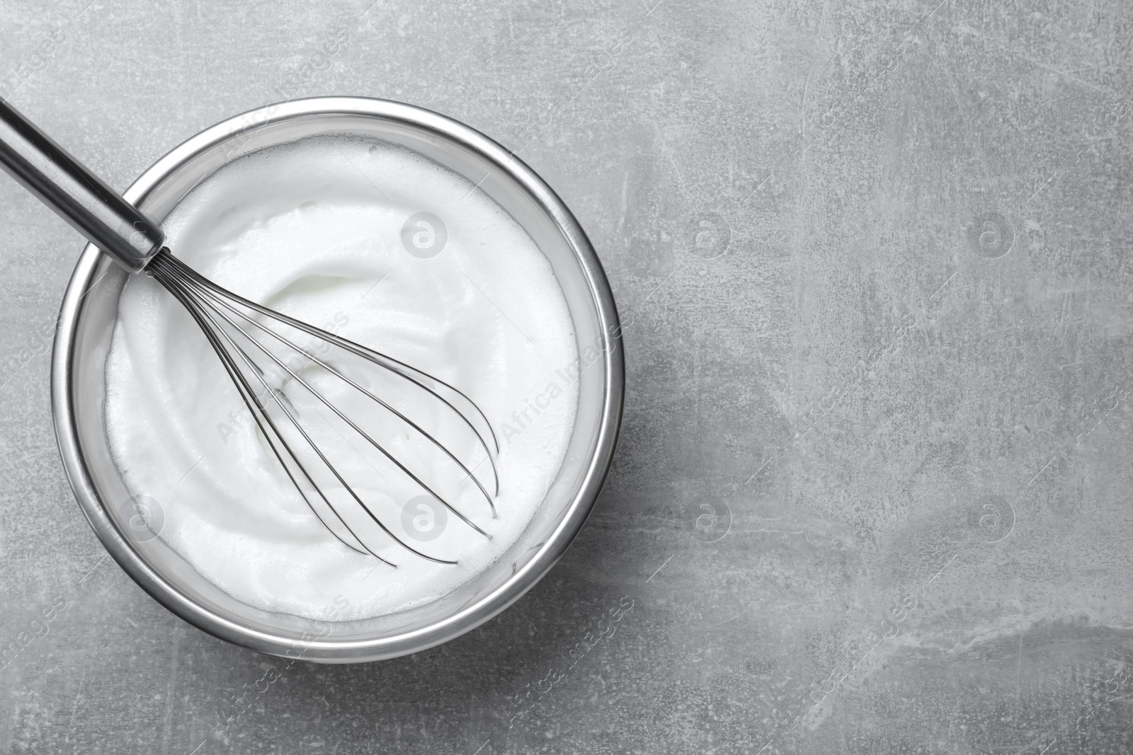 Photo of Whipped egg whites with balloon whisk on grey table, top view. Space for text