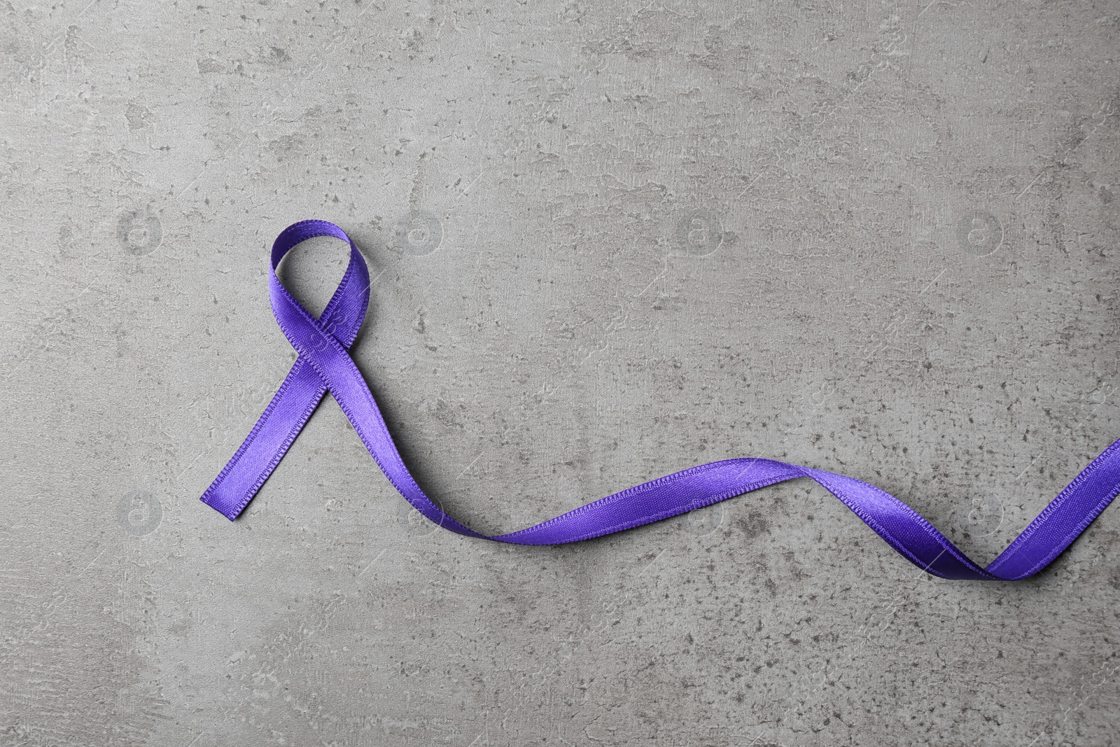 Photo of Purple ribbon on grey stone background, top view with space for text. Domestic violence awareness