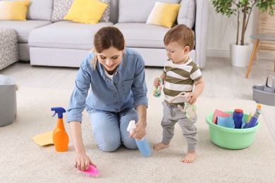 Photo of Housewife with little son cleaning carpet in room