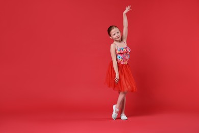 Photo of Cute little girl dancing on red background, space for text