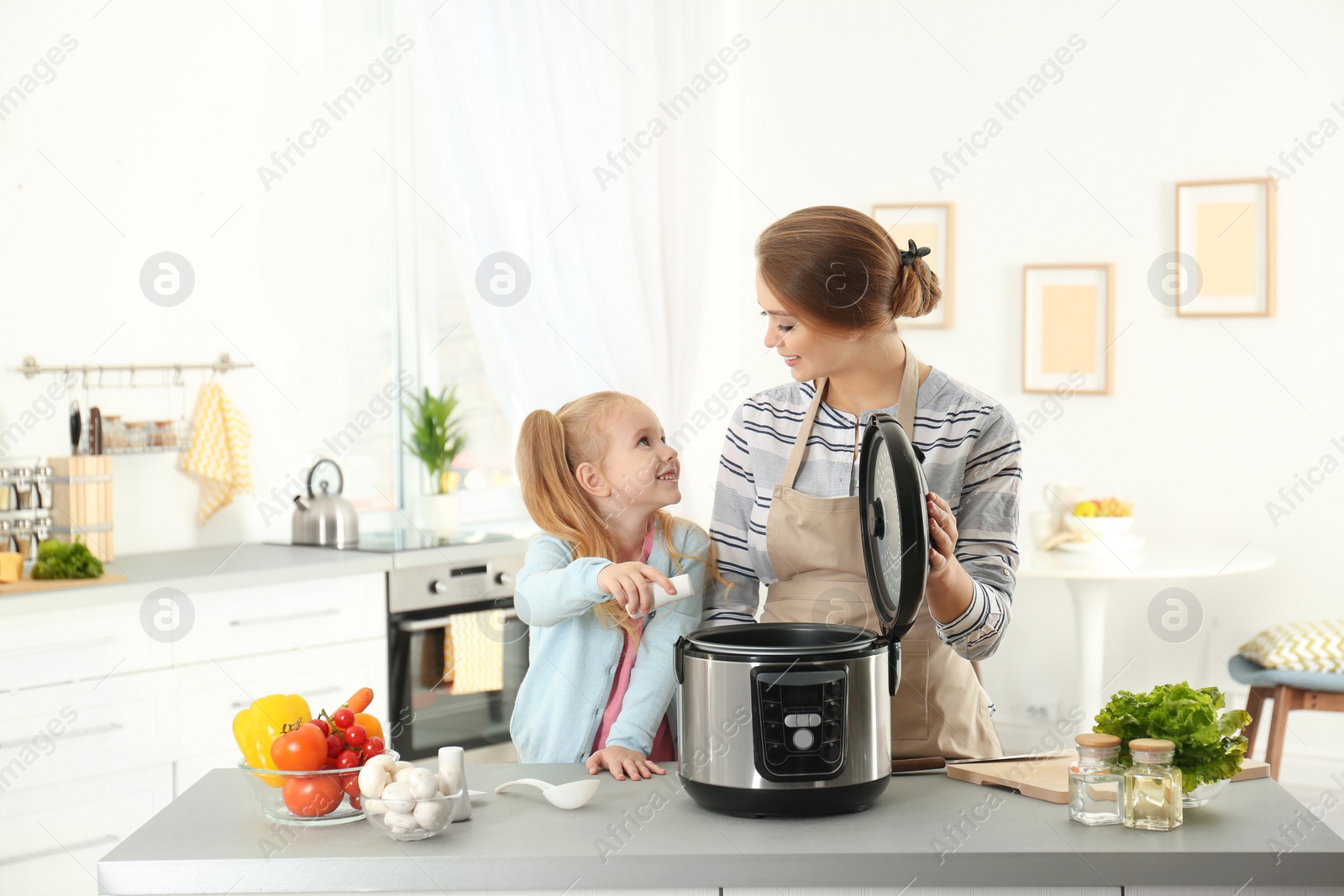 Photo of Mother and daughter preparing food with modern multi cooker in kitchen