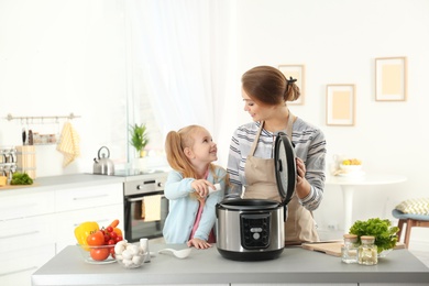 Photo of Mother and daughter preparing food with modern multi cooker in kitchen