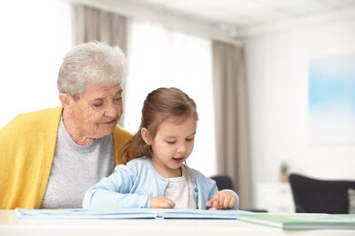 Cute girl and her grandmother reading book at home