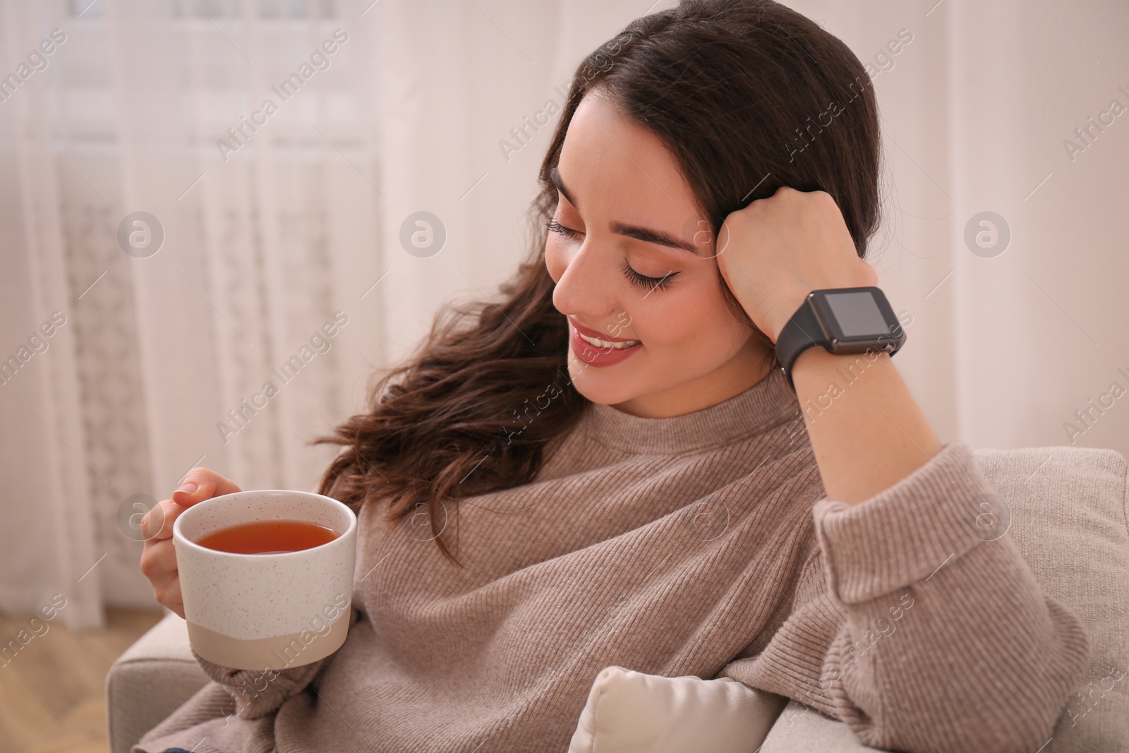 Photo of Young woman with smart watch and cup of tea at home