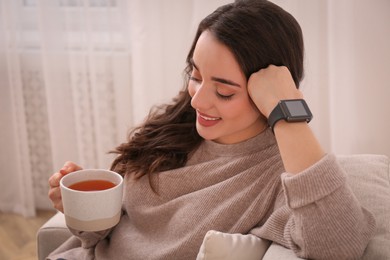 Young woman with smart watch and cup of tea at home