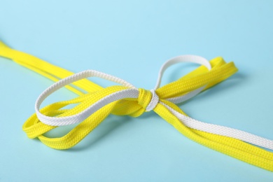 Photo of Yellow and white shoe laces tied in bow on light blue background, closeup