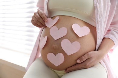 Photo of Pregnant woman with heart shaped sticky notes on belly indoors, closeup. Choosing baby name