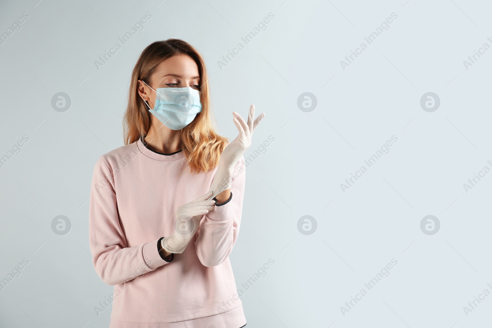 Photo of Young woman in protective mask putting on medical gloves against grey background. Space for text