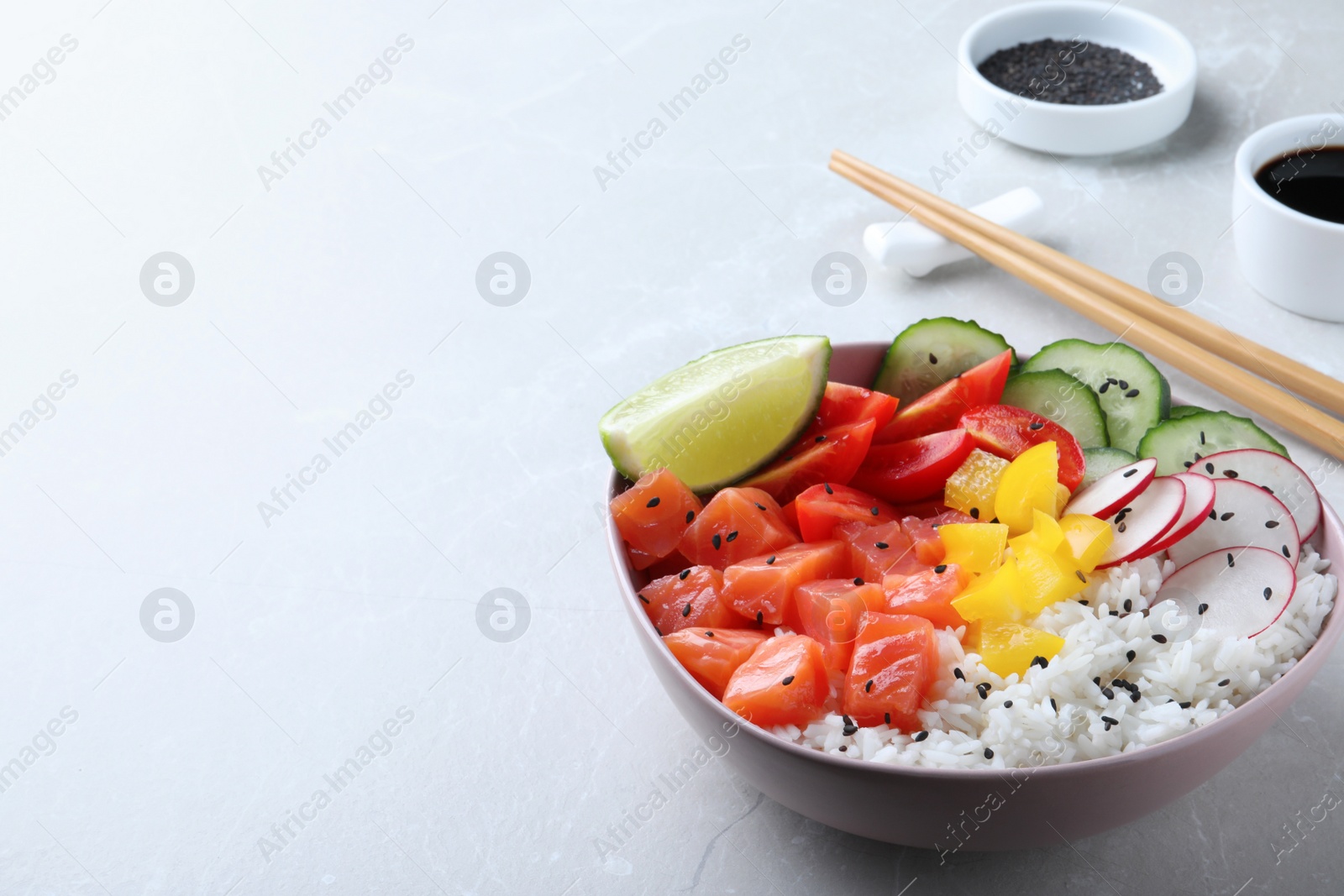 Photo of Delicious poke bowl with salmon, rice and vegetables served on light grey table. Space for text