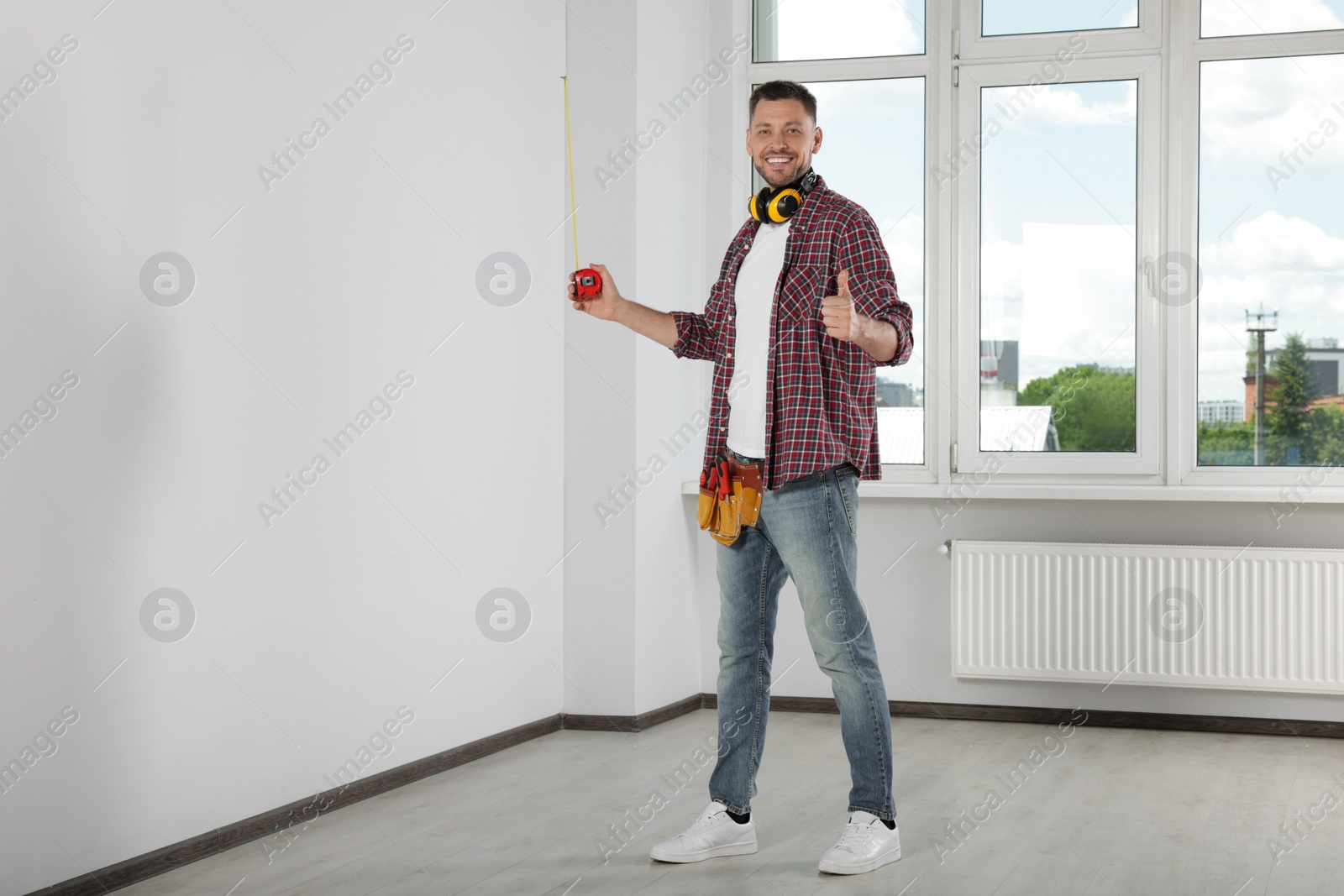 Photo of Handsome worker with measuring tape in empty room, space for text