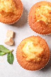 Delicious sweet muffins and brown sugar on light grey textured table, flat lay