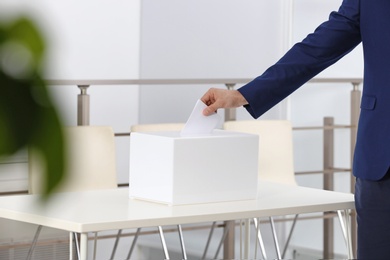 Man putting his vote into ballot box at polling station, closeup. Space for text